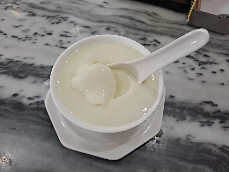 A bowl of double skin milk with a spoon lifting the skin